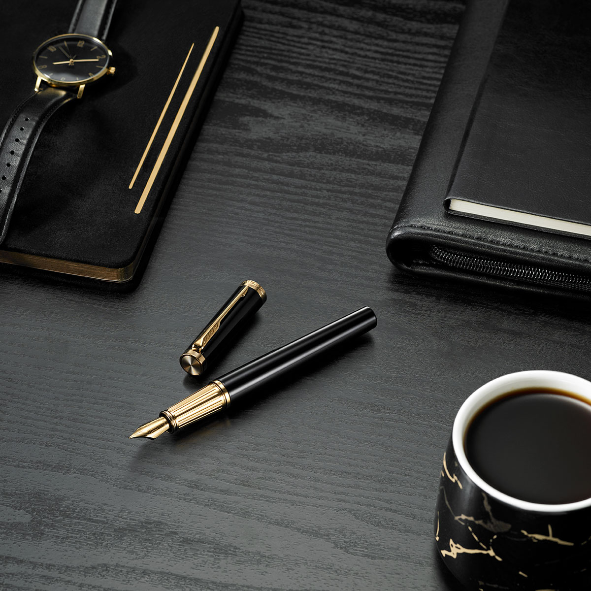 Czarne pióro wieczne Parker z pozłacanym wykończeniem na eleganckim biurku – obok skórzany notes, zegarek i filiżanka kawy w czarno-złotym kubku.